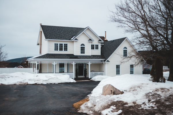 Two-story white suburban house with a front porch and black roof in winter with snow on the ground Two-story white suburban house with a front porch and black roof in winter with snow on the ground