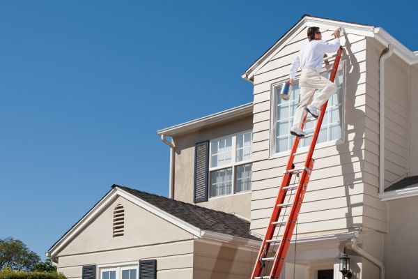 Professional painter on a ladder painting the exterior siding of a two-story house Professional painter on a ladder painting the exterior siding of a two-story house