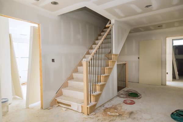 Interior home under construction with unfinished drywall and a wooden staircase installation Interior home under construction with unfinished drywall and a wooden staircase installation