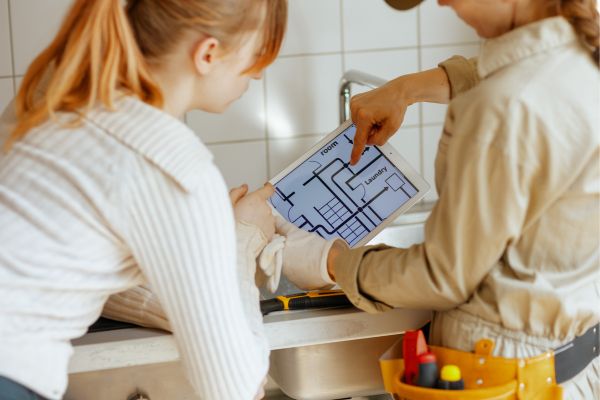 Contractor showing a homeowner a digital floor plan on a tablet during a home renovation consultation. Contractor showing a homeowner a digital floor plan on a tablet during a home renovation consultation.
