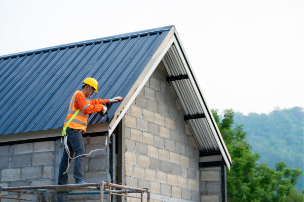 Construction worker in safety gear installing a metal roof on a new building Construction worker in safety gear installing a metal roof on a new building