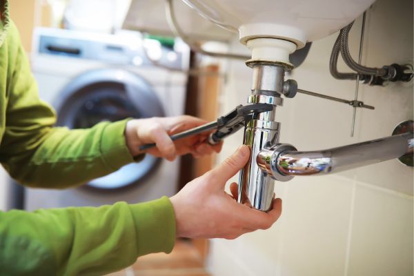 Plumber fixing a sink pipe with a wrench in a residential bathroom or laundry room Plumber fixing a sink pipe with a wrench in a residential bathroom or laundry room
