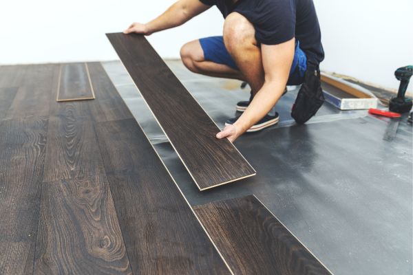 Worker installing dark wood laminate flooring in a modern home Worker installing dark wood laminate flooring in a modern home