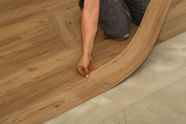 Installer placing a vinyl plank over adhesive underlayment during a flooring installation. Installer placing a vinyl plank over adhesive underlayment during a flooring installation.