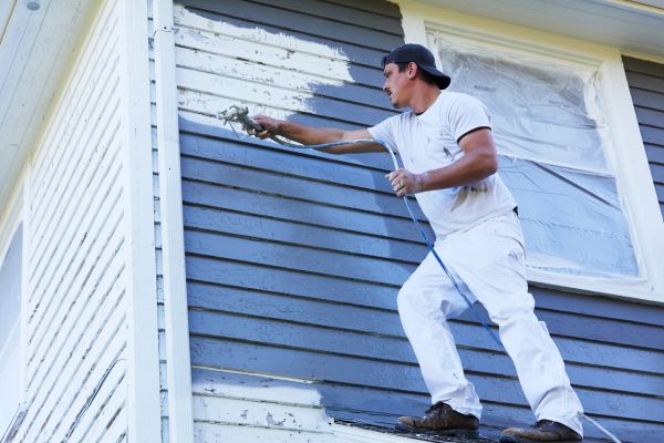 Painter using a sprayer to apply new paint to the exterior siding of a house. Painter using a sprayer to apply new paint to the exterior siding of a house.